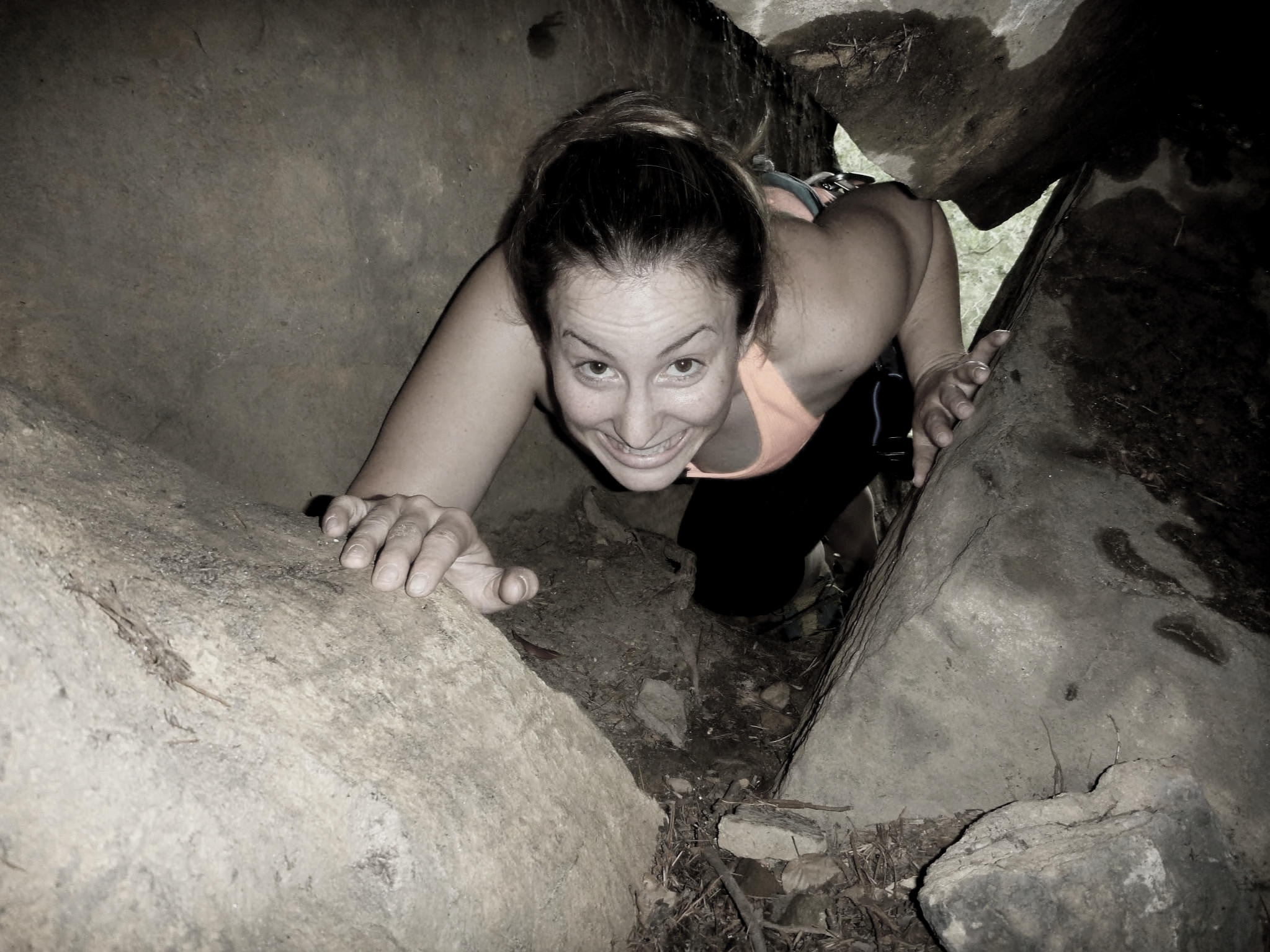 A woman crawling through a narrow, rocky tunnel with dirt walls, looking up and smiling at the camera. Caver's Route Red Rock Kentucky