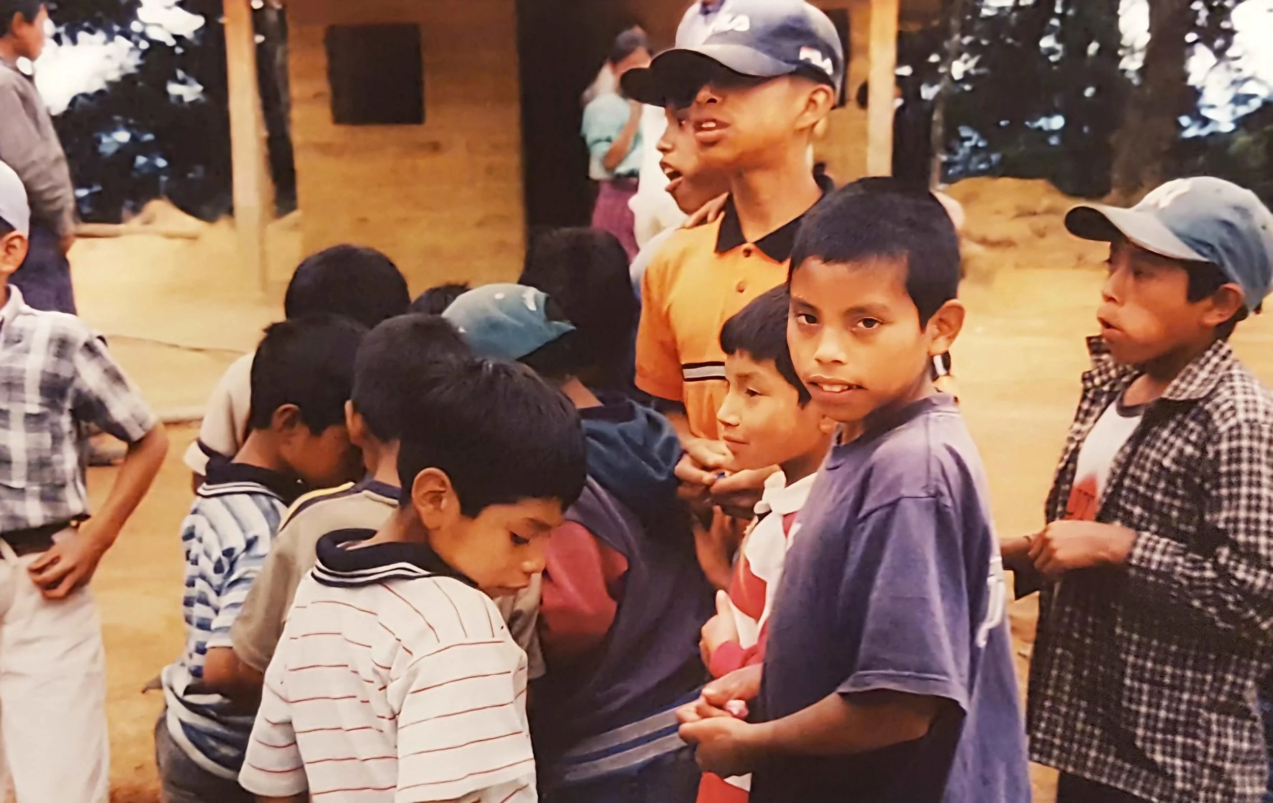 Kids and teenagers gathered indoors, some with eyes closed and heads bowed, participating in a prayer circle or group prayer.