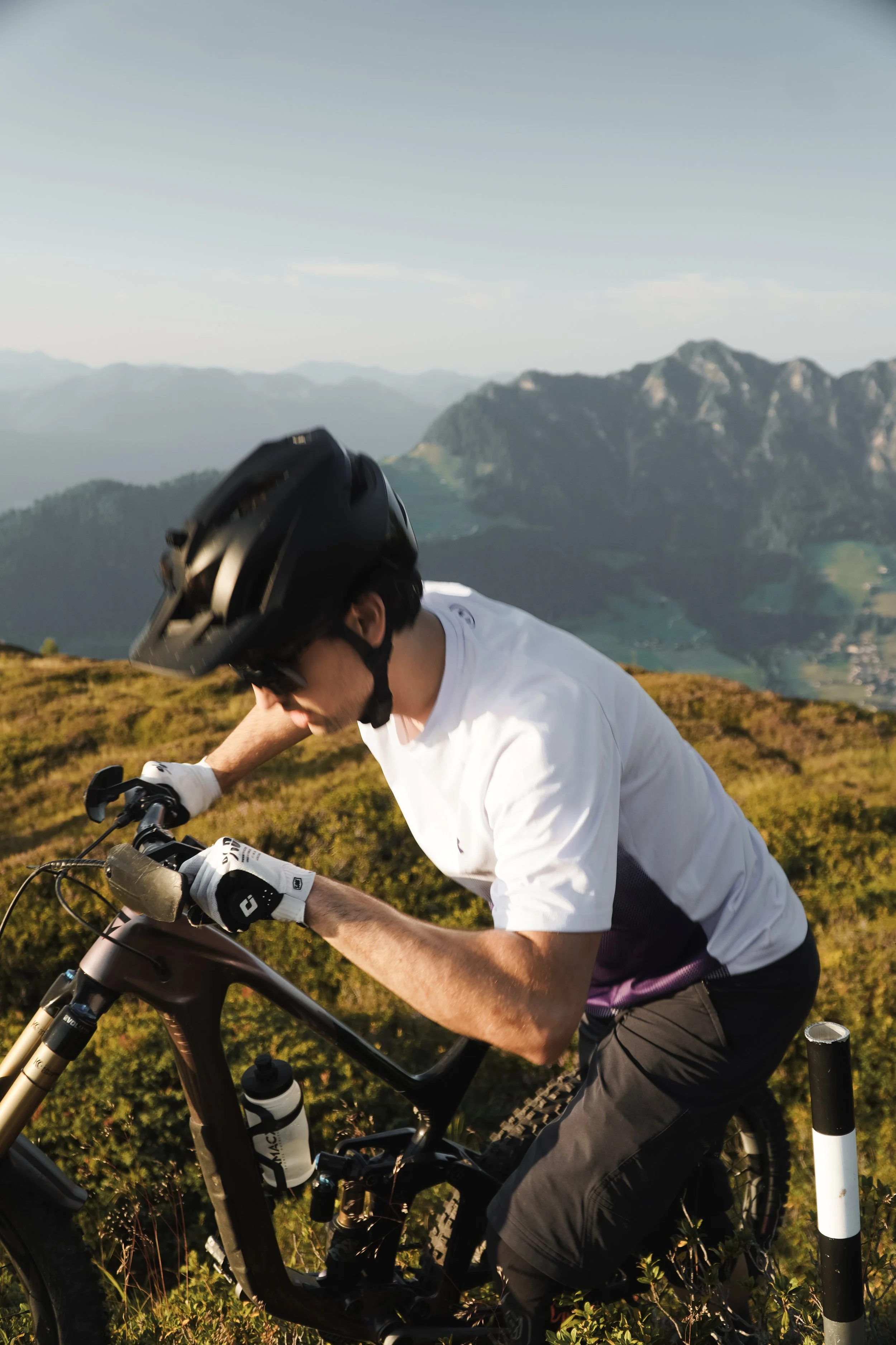 Mann fährt Mountainbike auf Bergpfad mit Bergkette im Hintergrund.