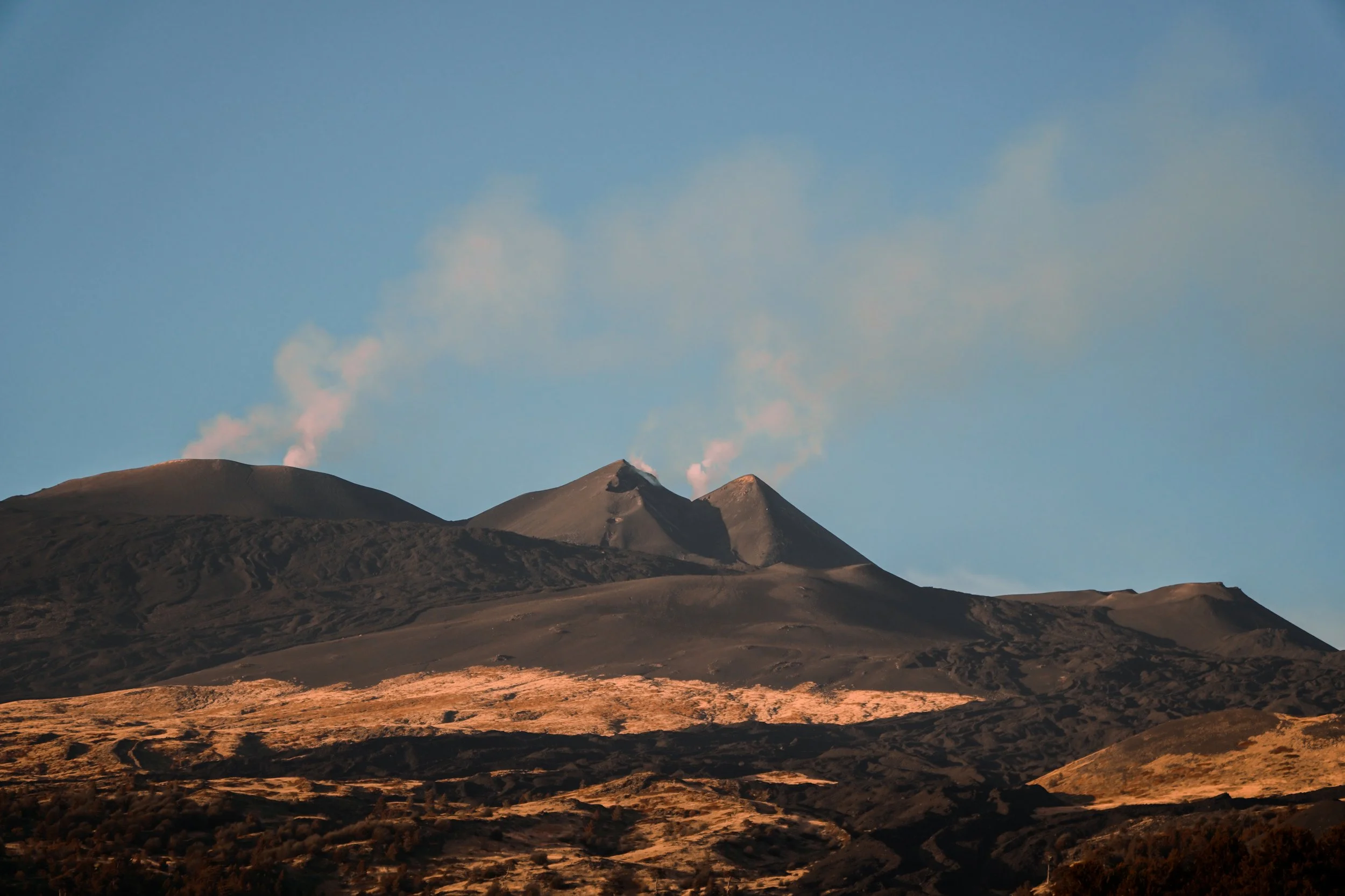 Vulkan mit dunklem, rauchendem Gipfel und blauer Himmel im Hintergrund.