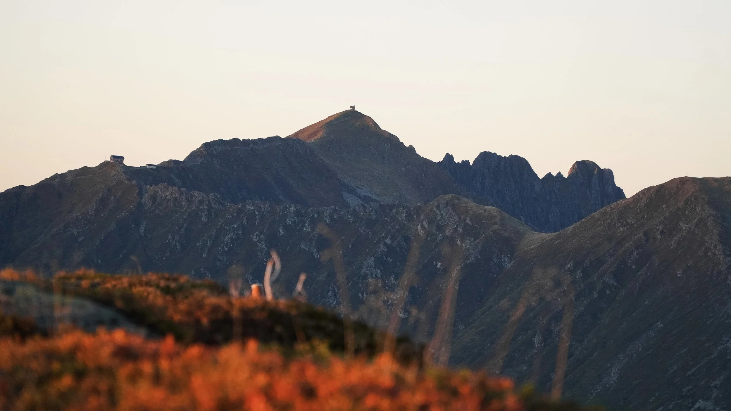 Bergpanorama mit Gipfeln, im Hintergrund Himmel bei Sonnenuntergang, im Vordergrund Herbstvegetation in warmen Tönen.