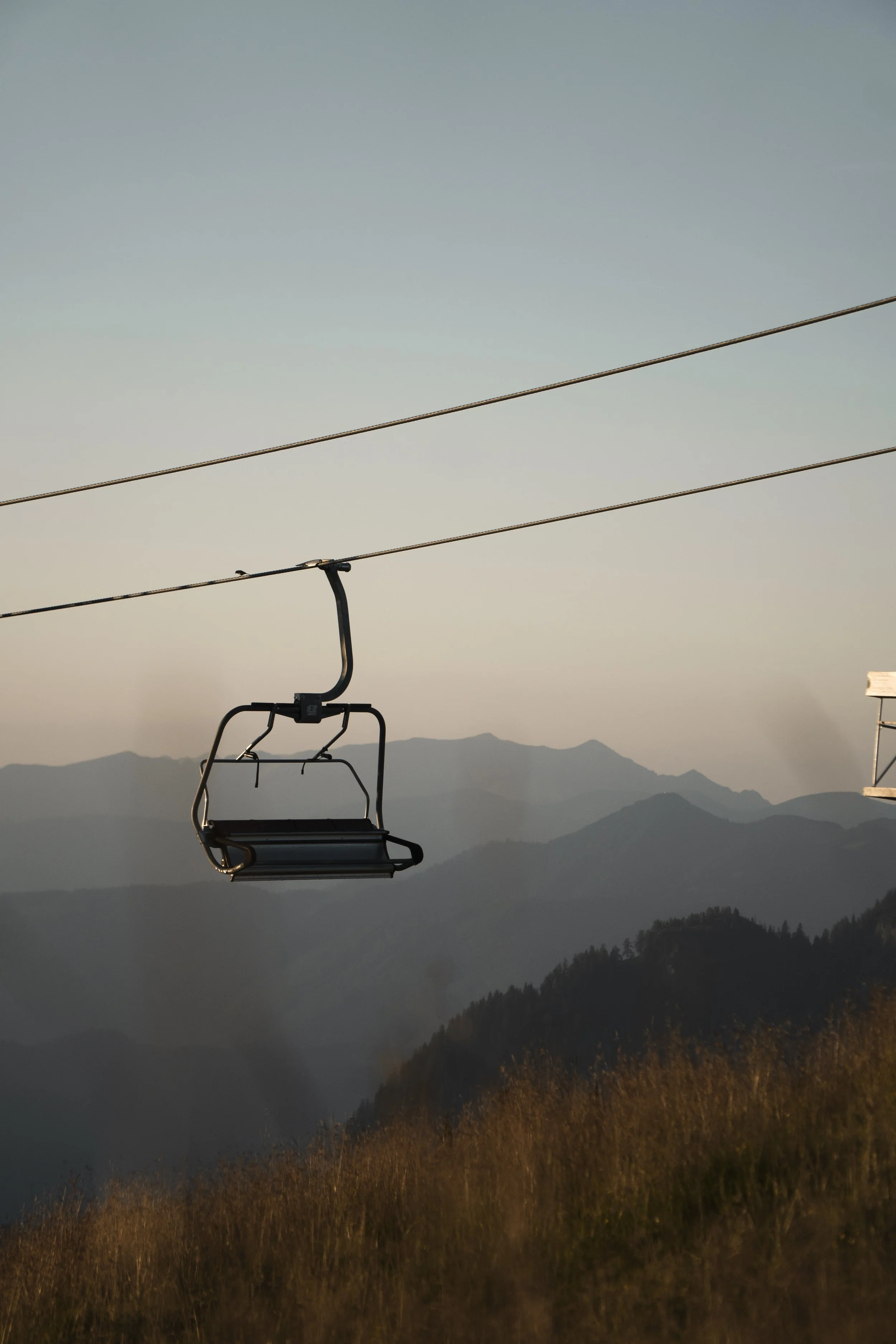 Ein leeres Skilift-Sitz hängt an einer Seilbahn vor einer Bergkulisse bei Sonnenuntergang.