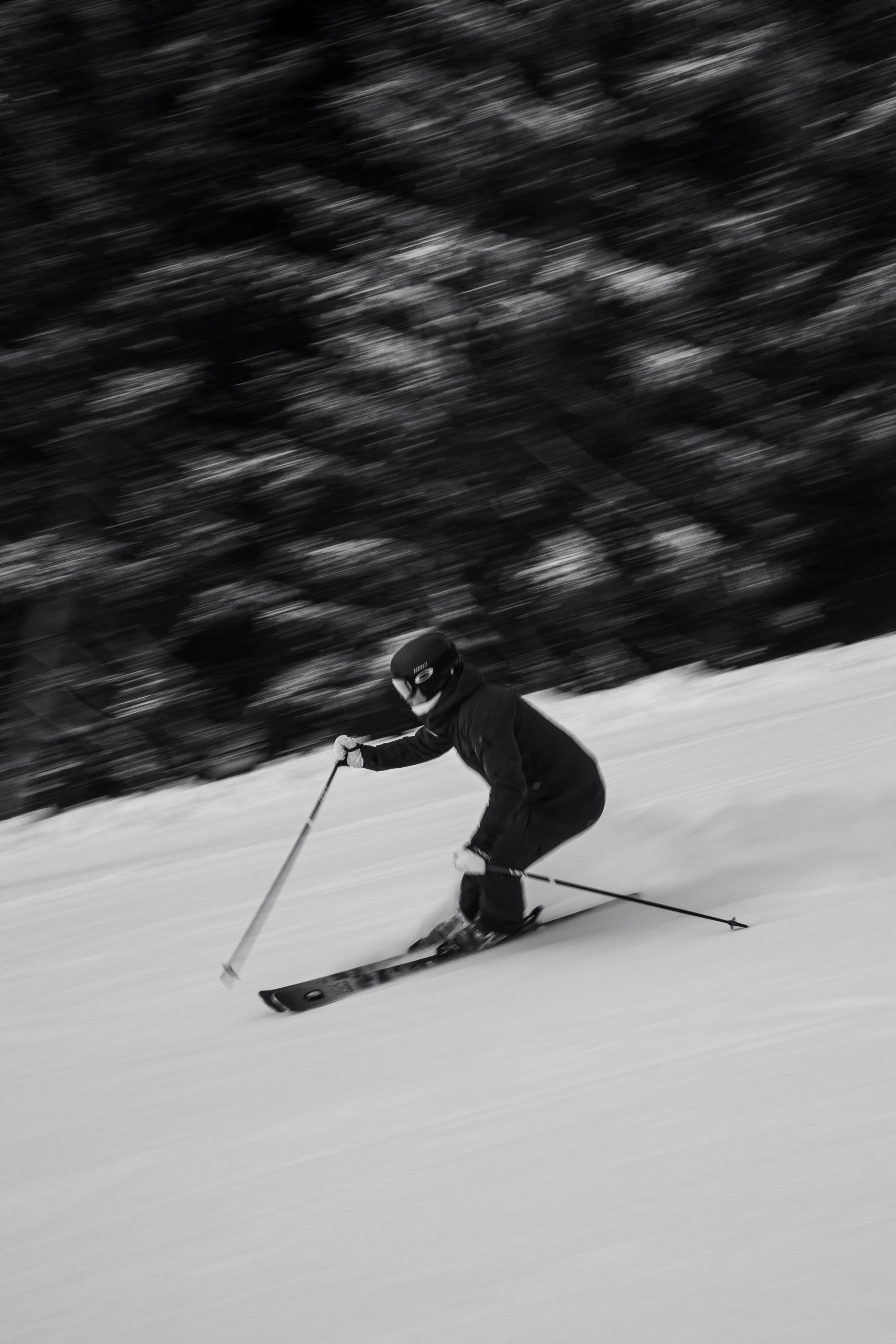 Ein Skifahrer in dunkler Kleidung, Helm und Skibrille, beim schnellen Abfahrtslauf auf einer schneebedeckten Piste.