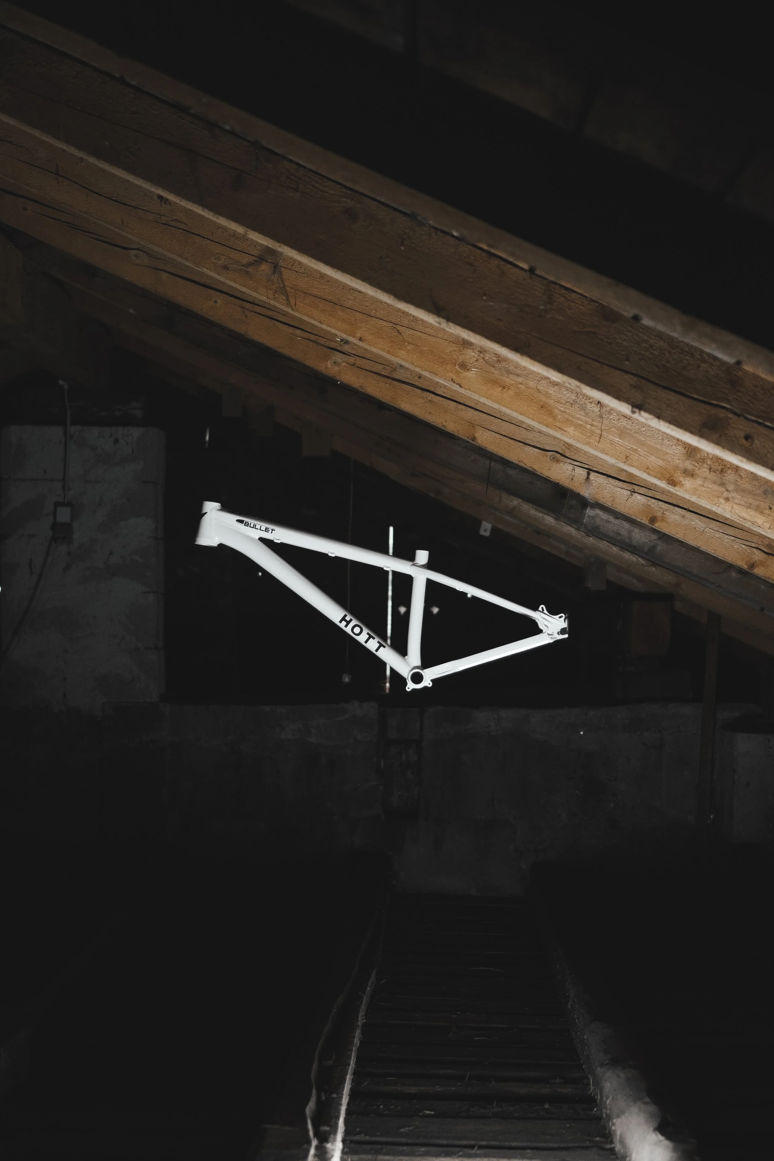 Weißes Fahrradrahmen schwebt an der Decke im dunklen Dachboden mit Holzbalken.