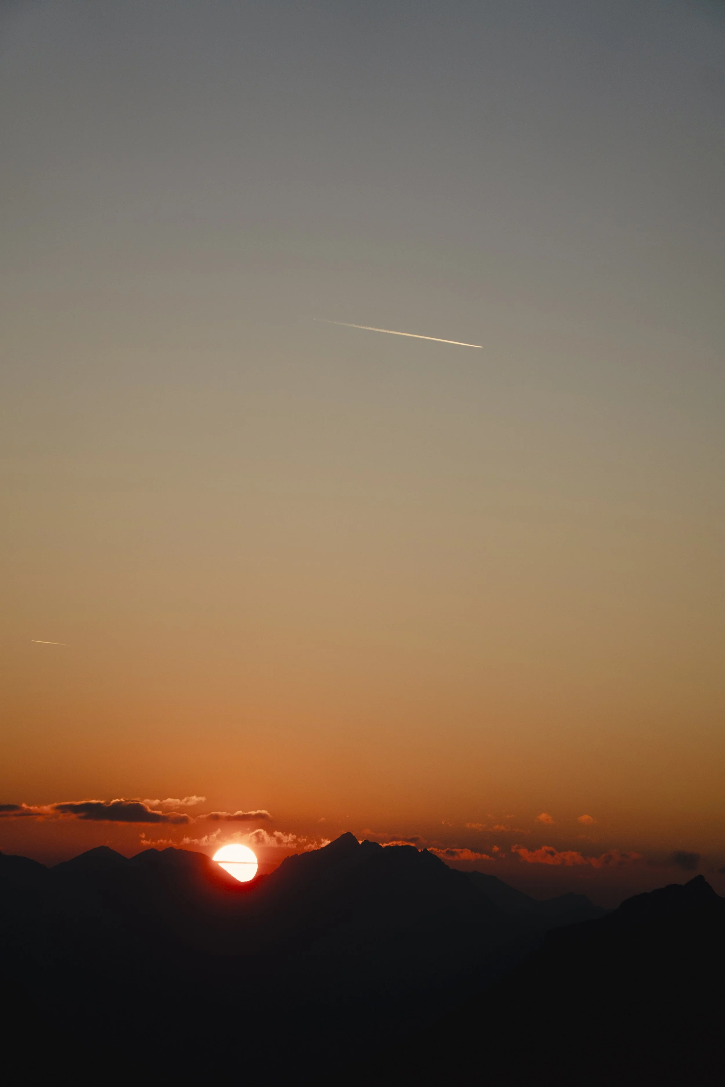 Sonnenuntergang hinter Berggipfeln, klare Himmel mit zwei Satellitenkonstellationen und einer Wolke.