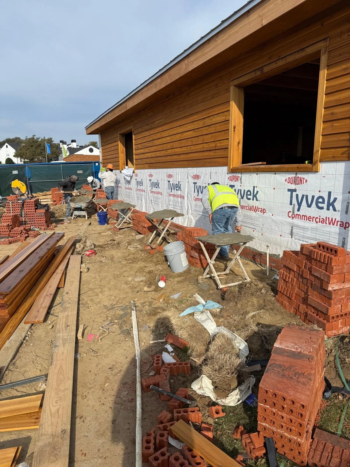 Construction workers building the exterior wall of a wooden house with brickwork and Tyvek weather barrier in progress.