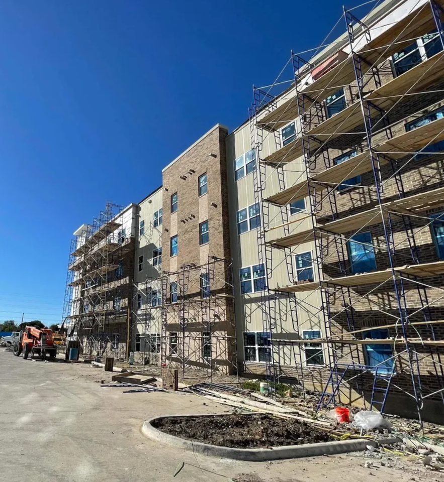 Construction site of a multi-story residential building with scaffolding and a construction truck on a clear, sunny day.