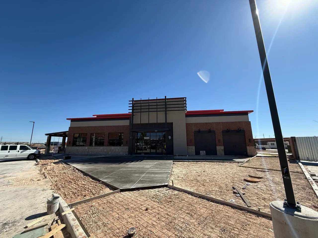 New fast-food restaurant under construction with a brick exterior and large glass entrance, surrounded by construction materials and dirt.