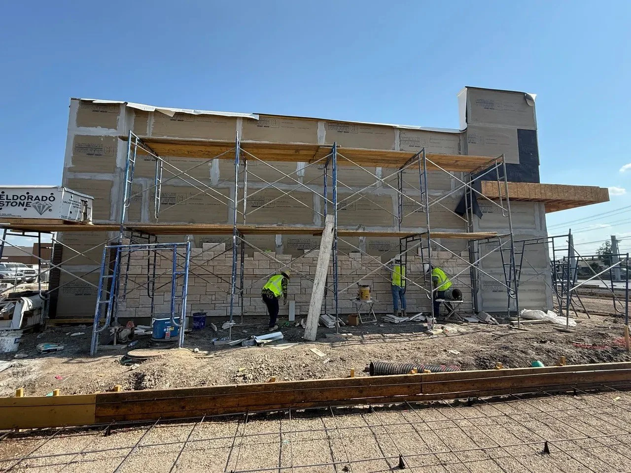 Construction workers building a house with scaffolding and brickwork, with a clear blue sky above.