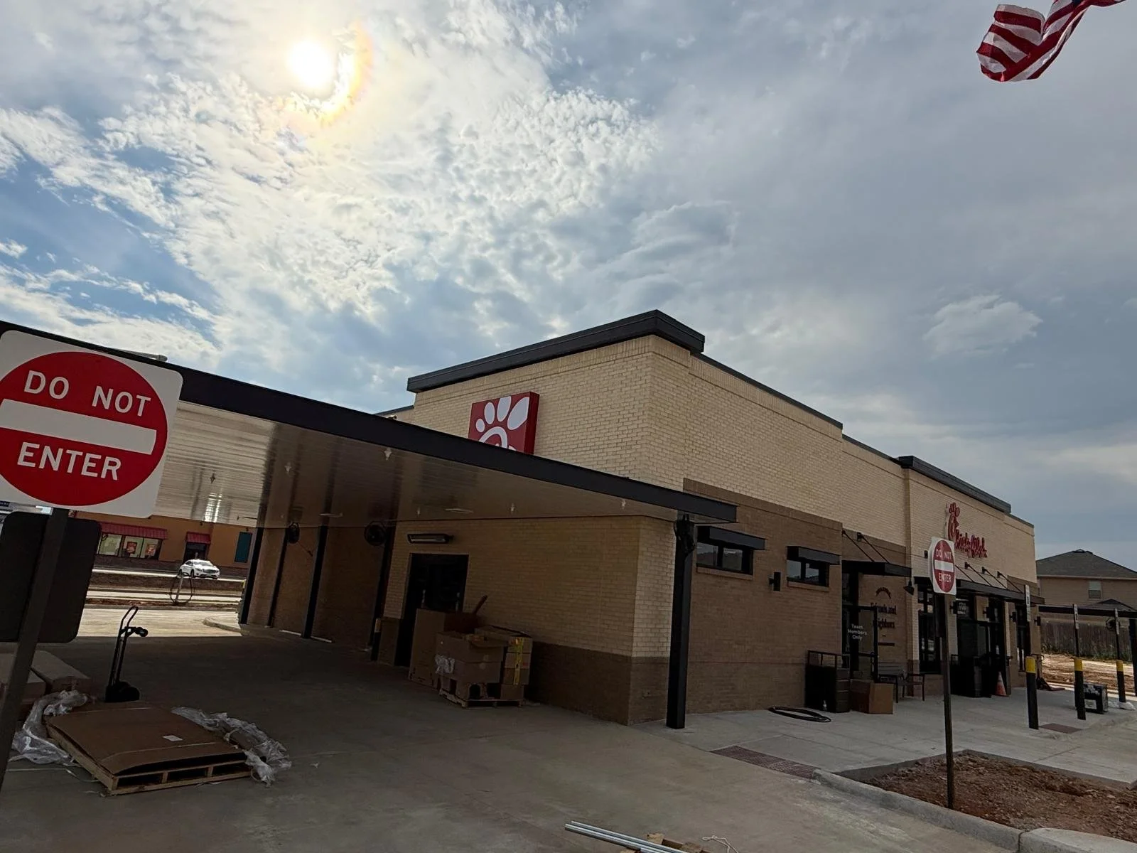 Chick-fil-A restaurant exterior under partly cloudy sky, with a large 'Do Not Enter' sign in the foreground, some construction materials and boxes on the ground.