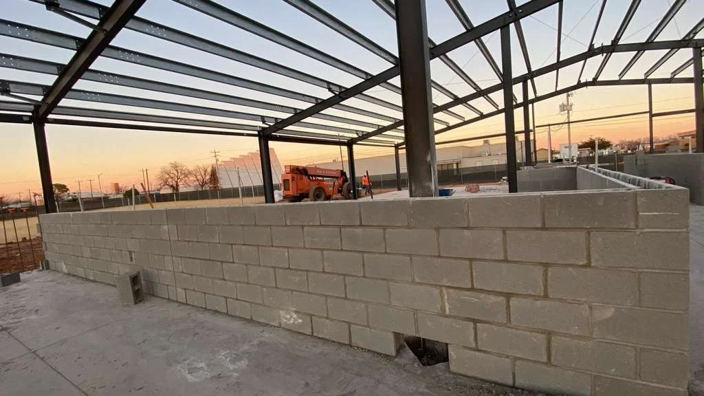 Construction site with a brick wall under a steel framework during sunset.