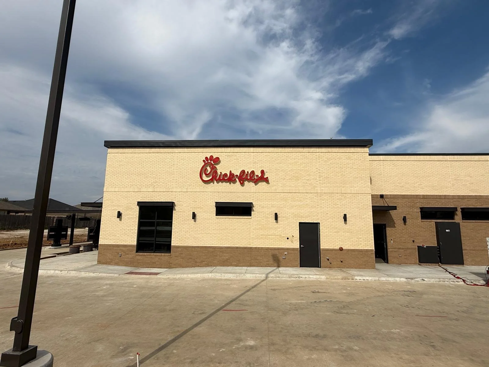 New Chick-fil-A restaurant under construction with the logo visible on the beige brick exterior, and some construction equipment and materials visible in the foreground.