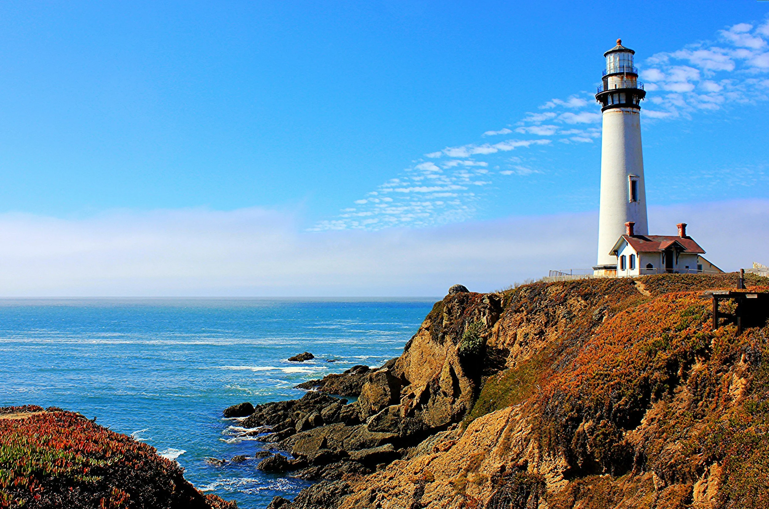 A lighthouse on a rocky cliff overlooking the Pacific Ocean. Lighthouse represents individual therapy journey, connecting with inner guide or inner healer within, heightened awareness, wisdom, and deeper intuitive understanding of one's self & world
