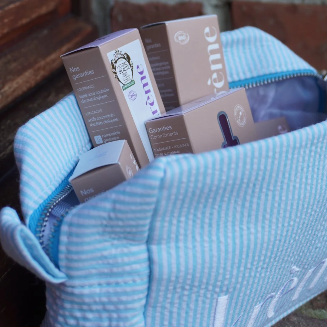 Une toile bleue à rayures blanches contient plusieurs boîtes de produits cosmétiques ou de soin, avec des inscriptions en français visibles sur les emballages.