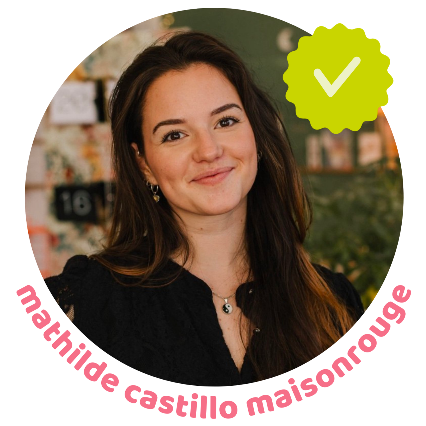 Une femme souriante portant un collier yin-yang, avec un fond flou et un badge vert avec une coche.