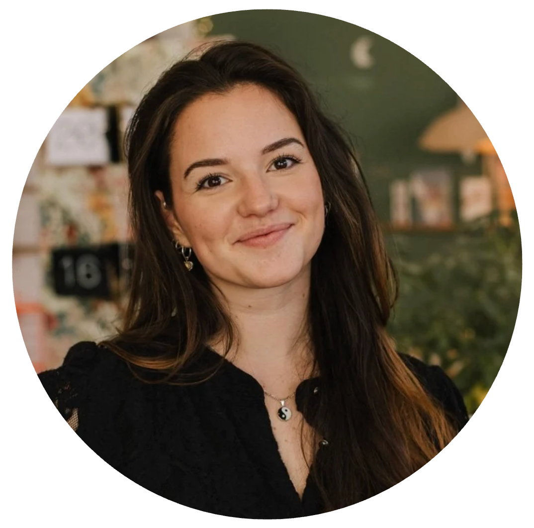 Une femme souriante avec de longs cheveux bruns, portant un collier yin-yang, dans un environnement intérieur confortable.
