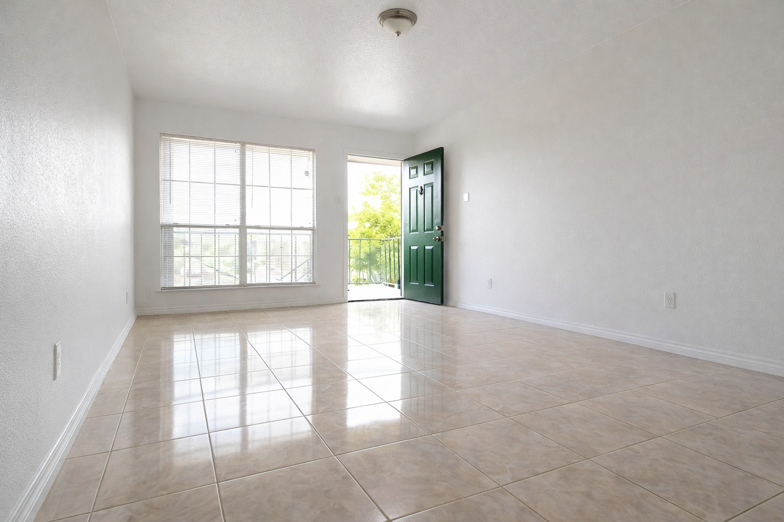 Bright, empty living room at Greyfield Apartments with tile flooring, a large window, and an open door leading to a private balcony