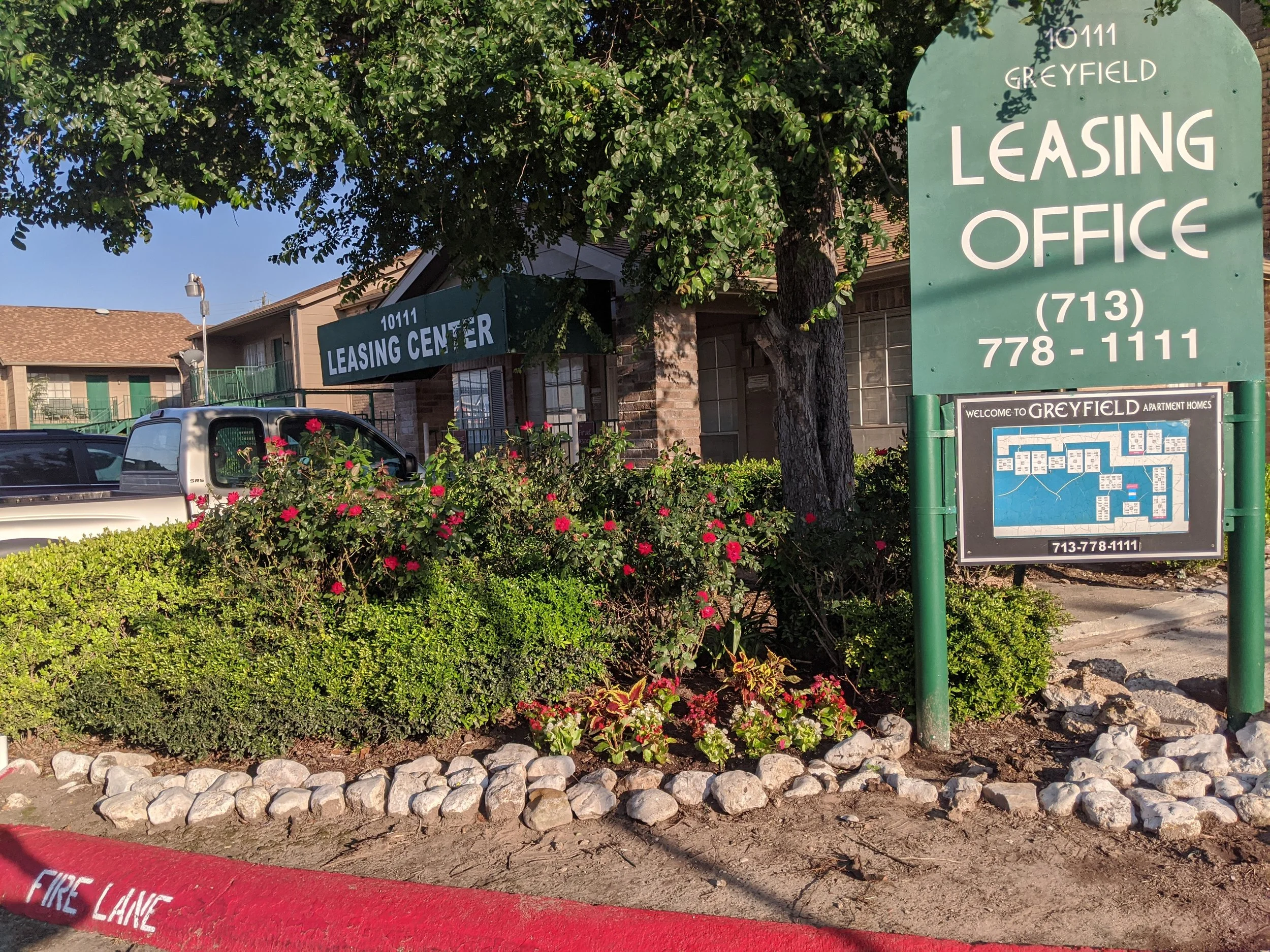 Greyfield Apartment Homes leasing office sign and entrance, framed by green landscaping. Phone: (713) 778-1111.