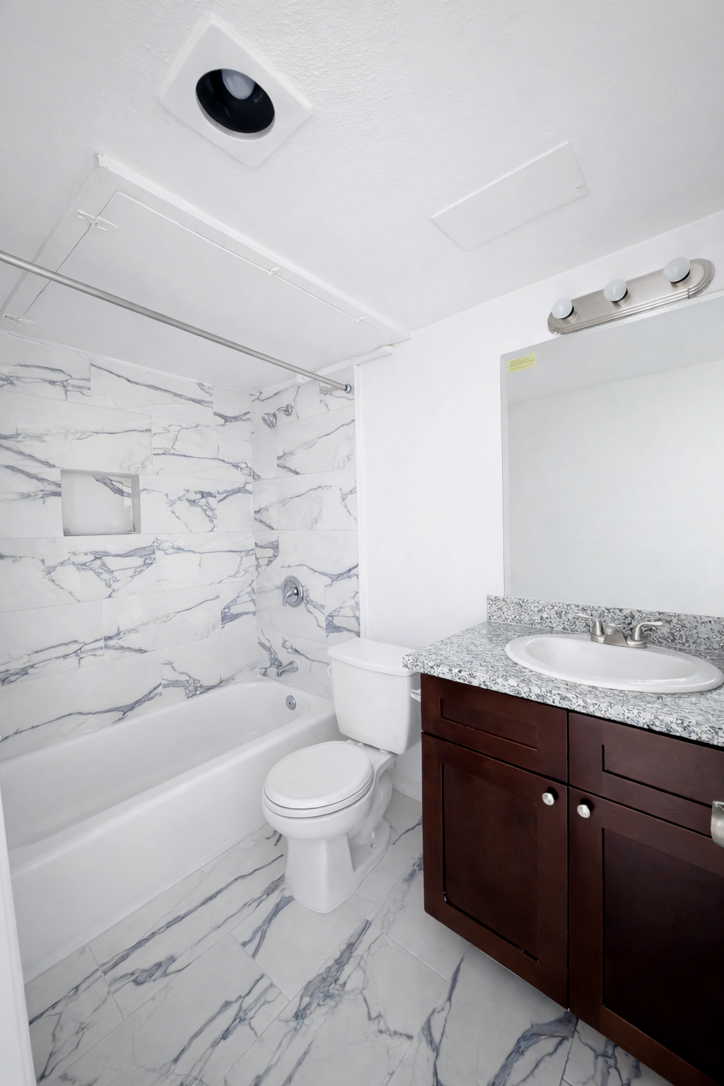 Bathroom at Greyfield Apartments with marble-style tile walls and floor, a soaking tub and shower, dark wood vanity, and granite countertop