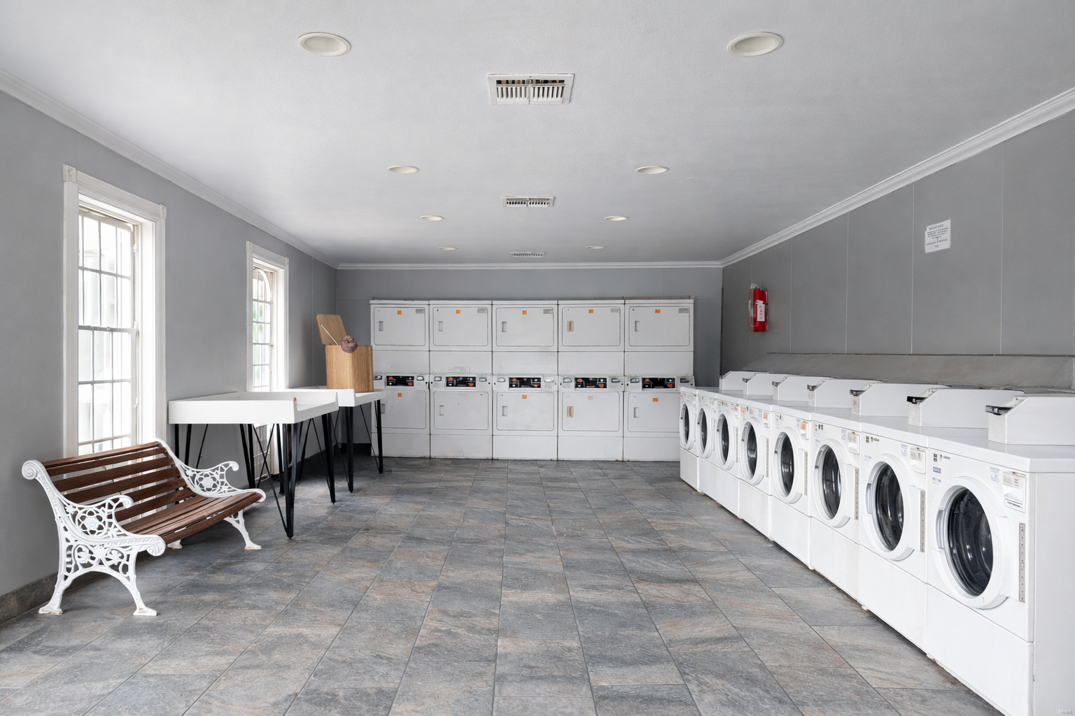 On-site laundry room at Greyfield Apartments with multiple washers and dryers, tile flooring, and a folding table