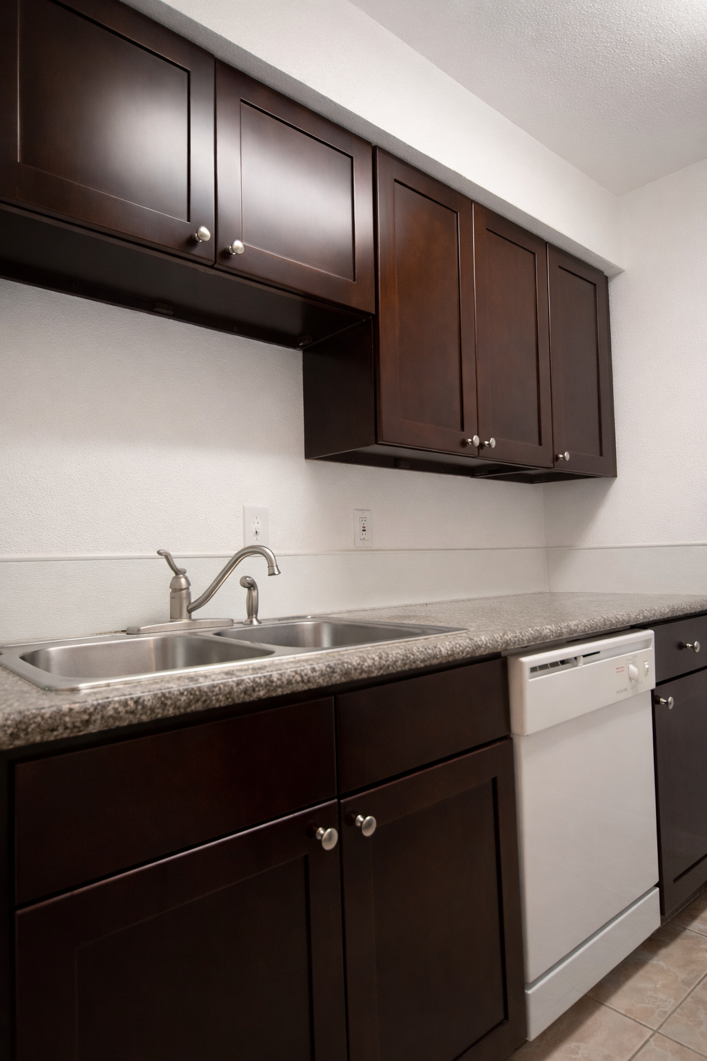 Kitchen at Greyfield Apartments with dark wood cabinets, a stainless steel double sink, granite-style countertops, and a built-in dishwasher