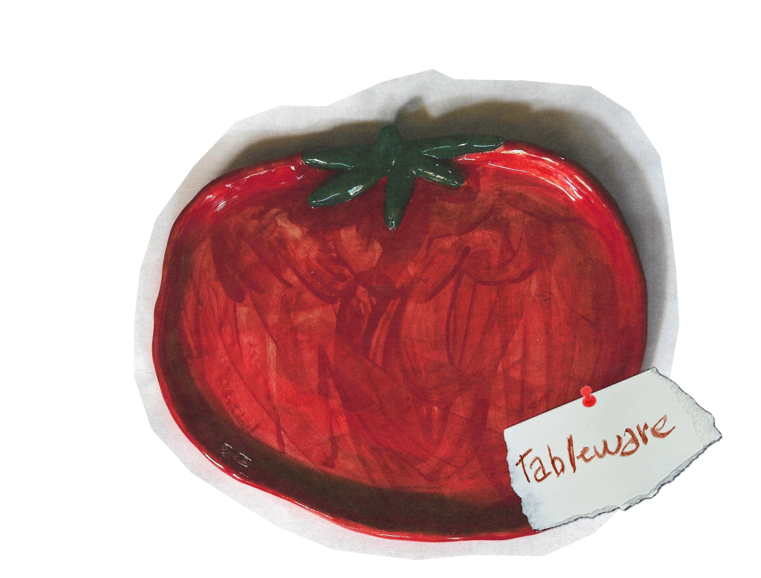 Close-up of a fruit-shaped object resembling a strawberry with a green leaf top and a white paper label attached to its bottom right that has red handwritten text. The object appears to be a decorative item or possibly a painted or textured surface.