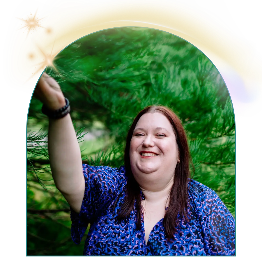 Woman with long dark hair smiling as she reaches out with her right arm in front of a lush green background.