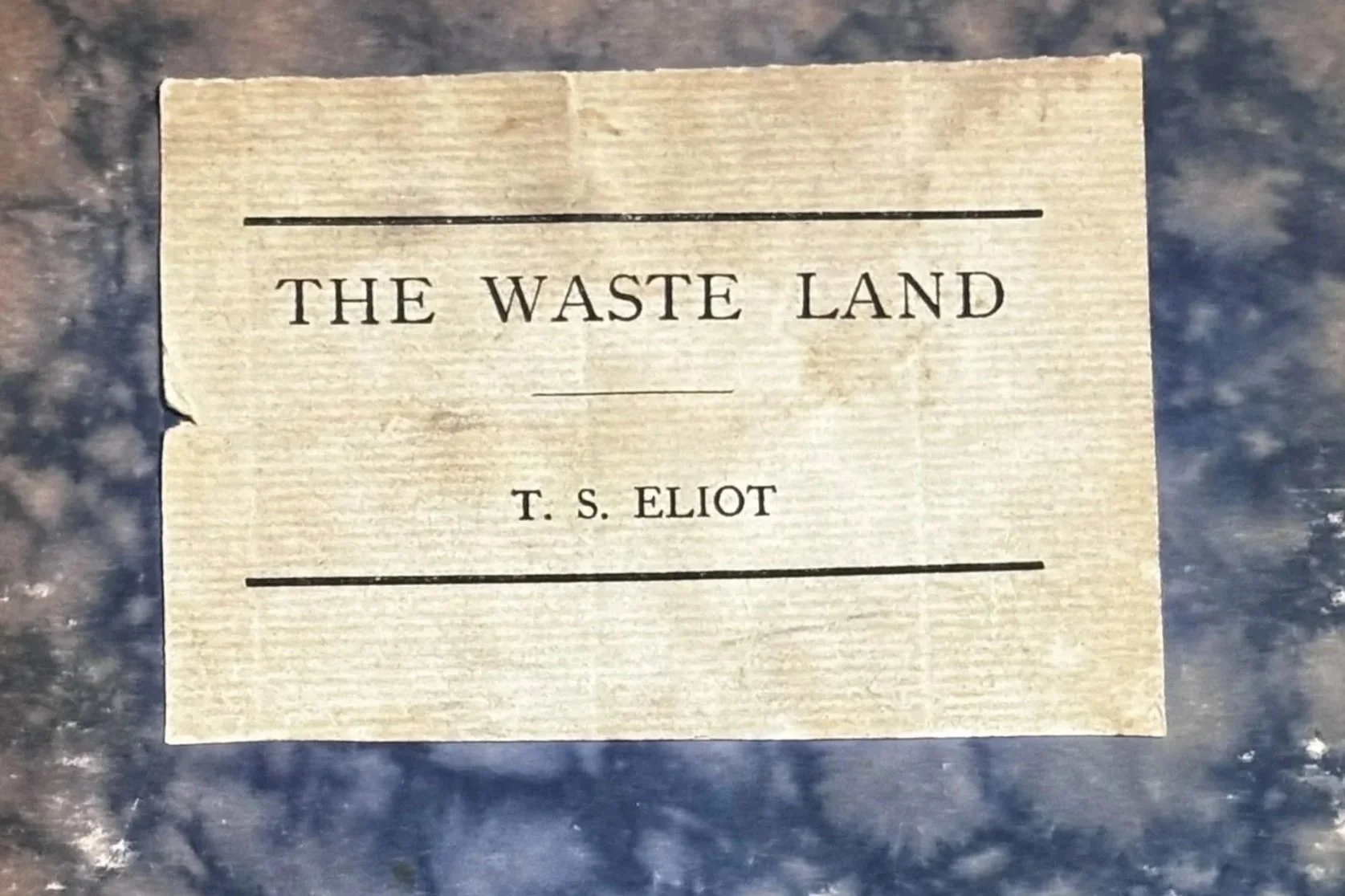 A paper label with the title 'The Waste Land' by T.S. Eliot laid on a dark, possibly marble, surface.