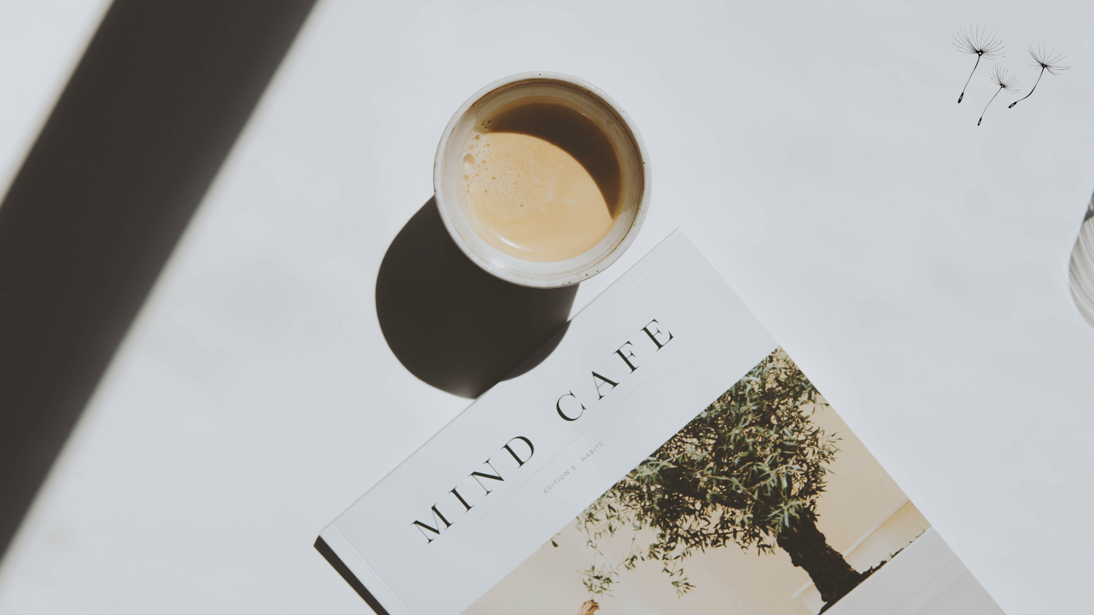 Cup of coffee on a shaddowy desk with a copy of 'mind cafe' magazine