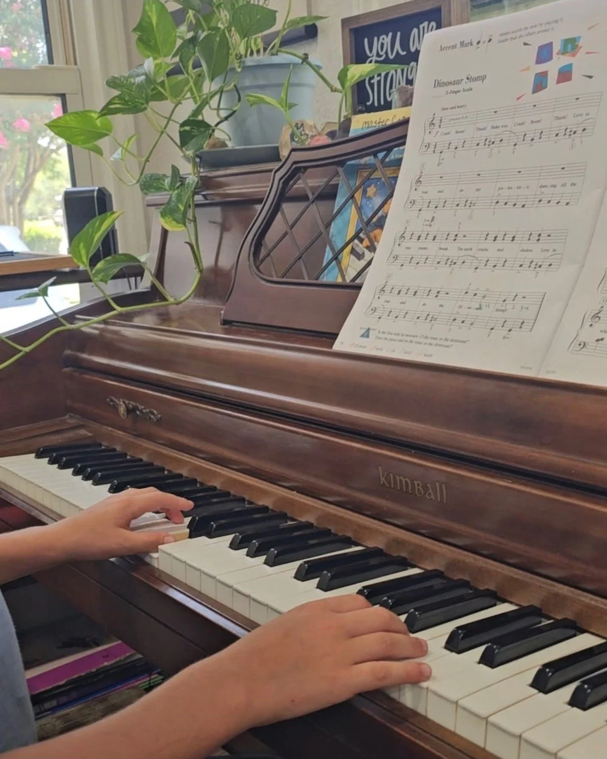 Young piano student’s hands practicing at an upright piano with a subtle Little Masterpiece Musicians watermark.