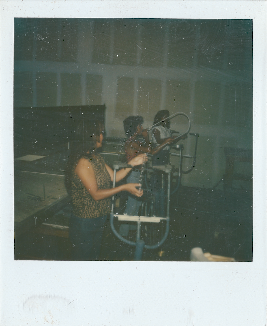 Two women in a recording studio, one adjusting a microphone and the other holding a glass, with a piano in the background.