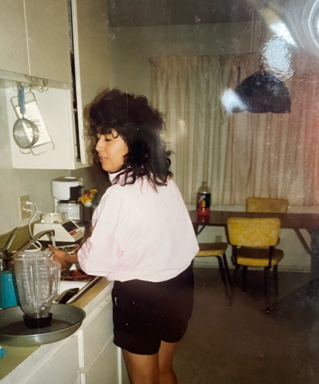 Woman with curly hair washing dishes in a kitchen, seen through a glass door