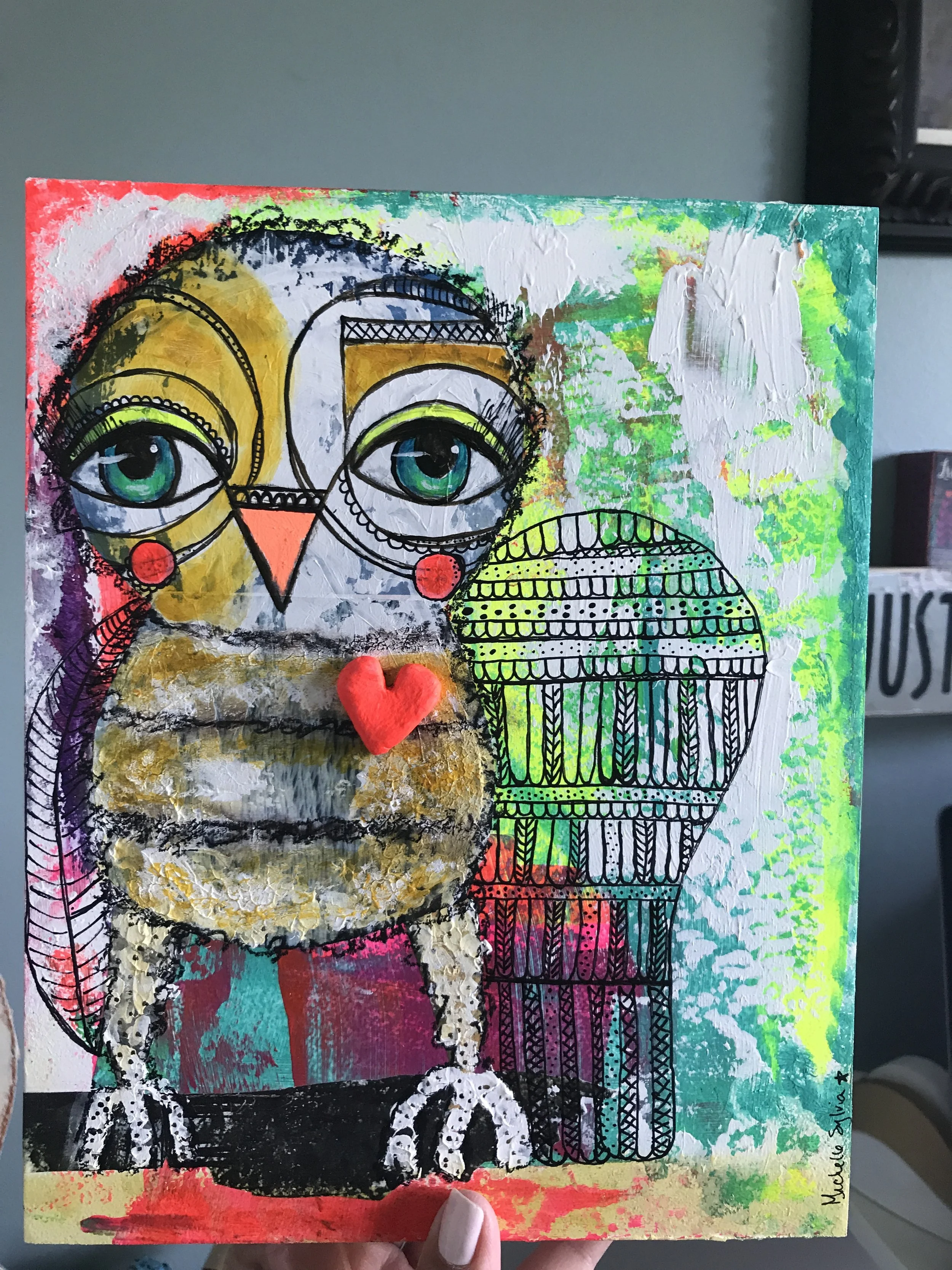 Colorful mixed media artwork of an owl with exaggerated eyes, large beak, and textured body, featuring black line drawings, vibrant background colors, and a small red heart-shaped object on its chest.