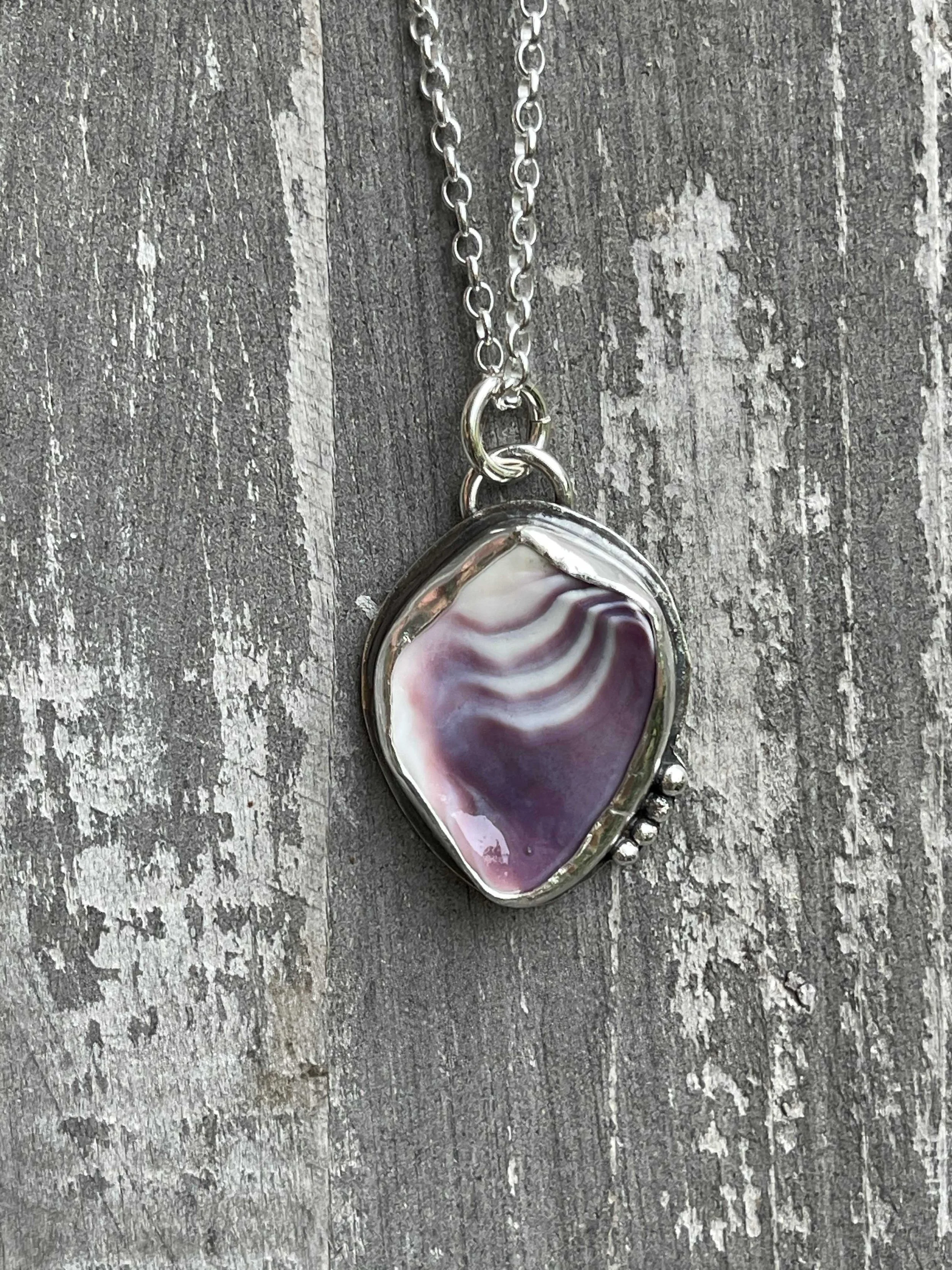 Silver necklace with a large, irregularly shaped purple and white striped agate pendant hanging on a weathered wooden surface.