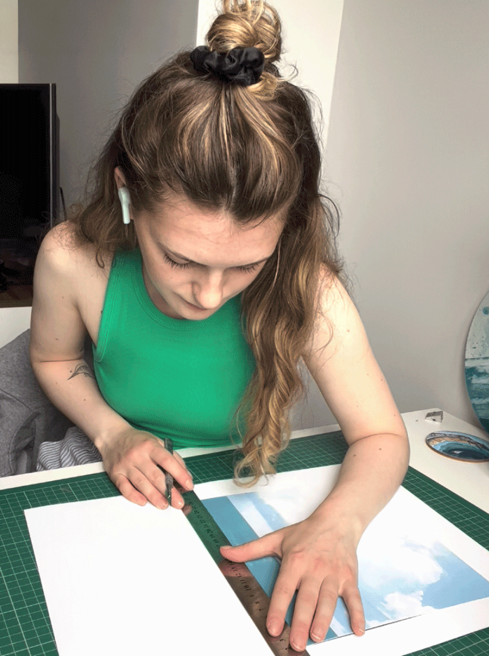 Woman measuring a piece of artwork with a ruler on a green cutting mat in an art studio.