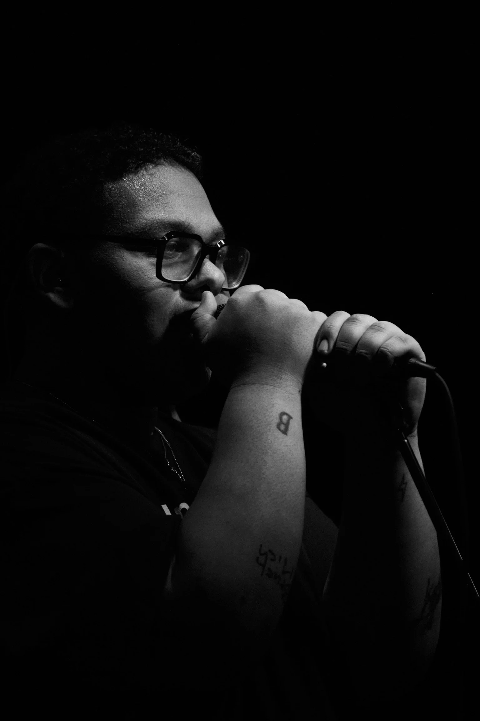 Mann mit Brille, der in ein Mikrofon singt, bei schwachem Licht aufgenommen, Schwarz-Weiß-Foto