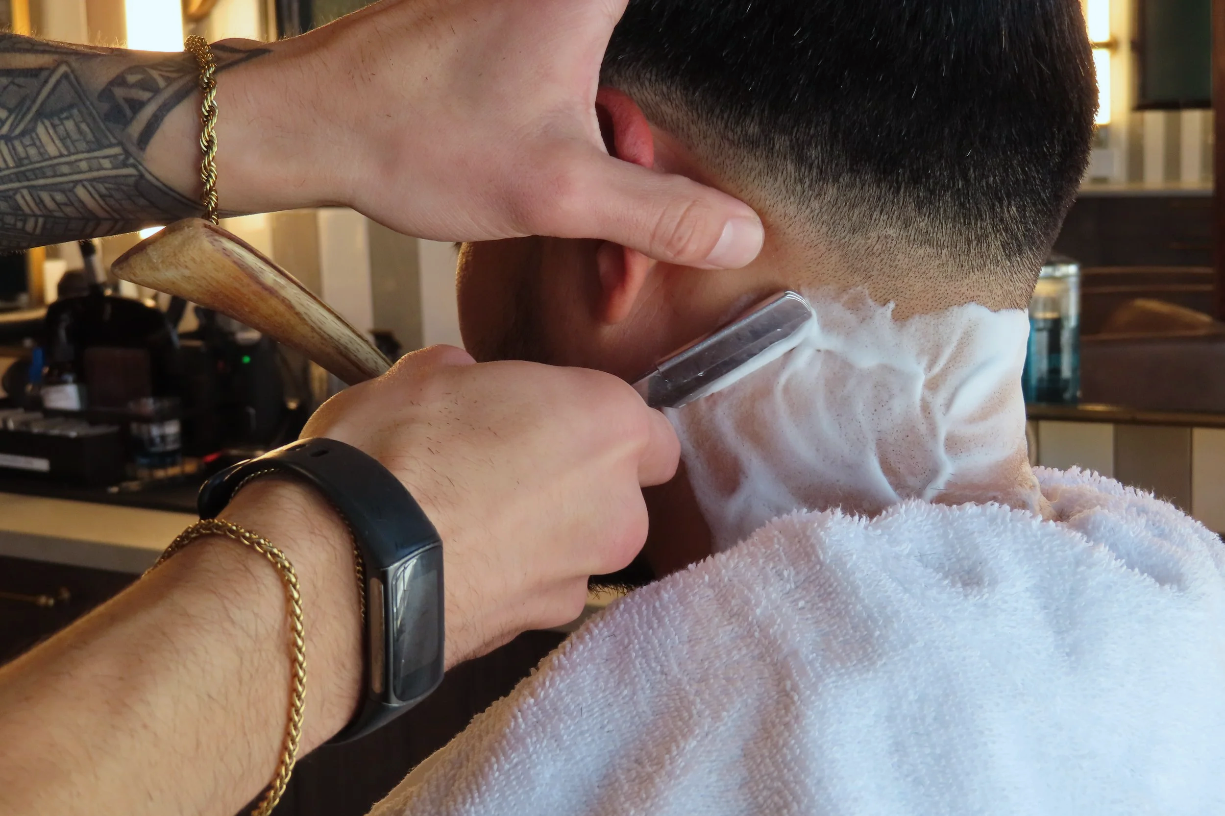 Barber shaving a man's neck with a straight razor, foam on the neck, client with a towel around the shoulders in a barbershop.