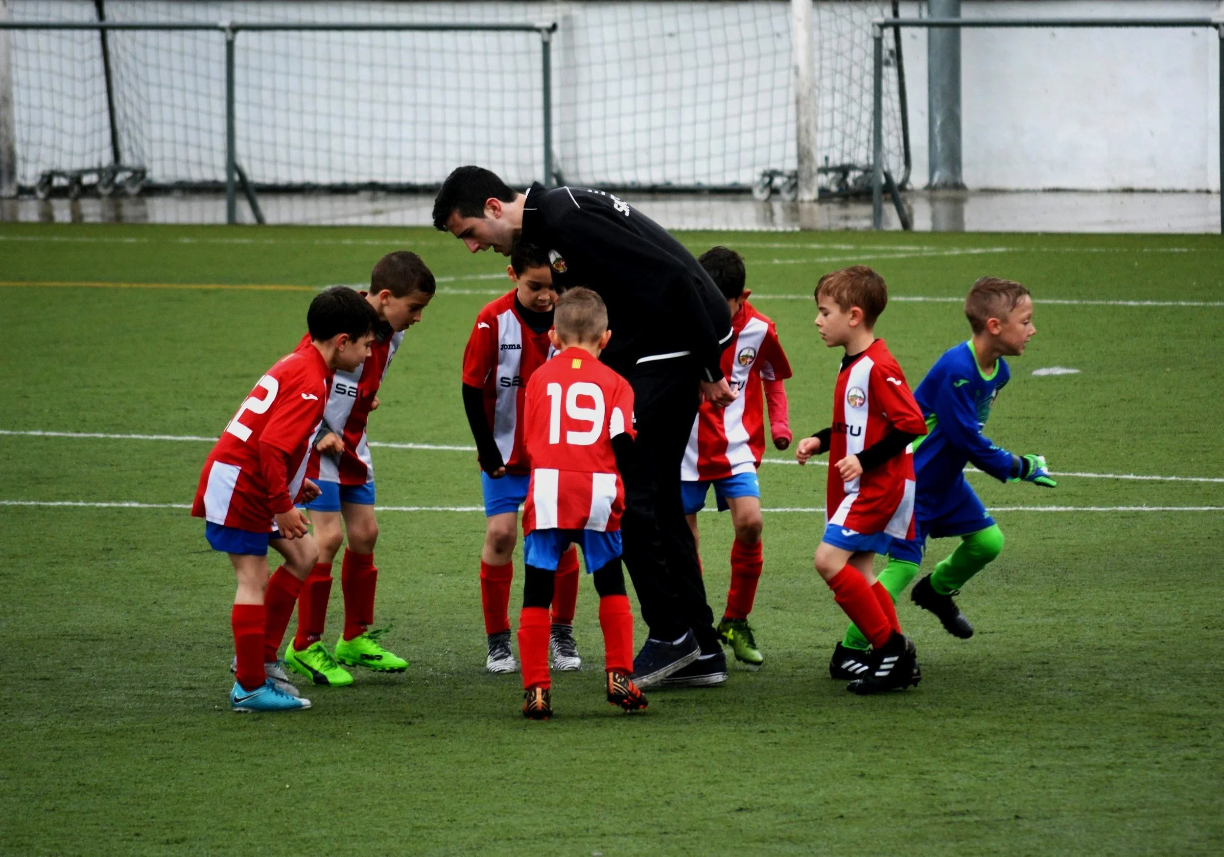 Young boys in soccer uniforms gathered around a coach on an indoor soccer field, preparing for a game.