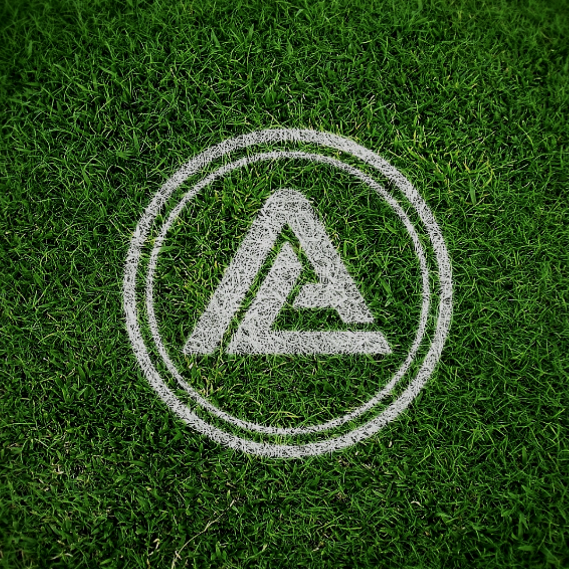 White chalk drawing of a triangle with an eye-like shape in the center, enclosed in a circle, on green grass.