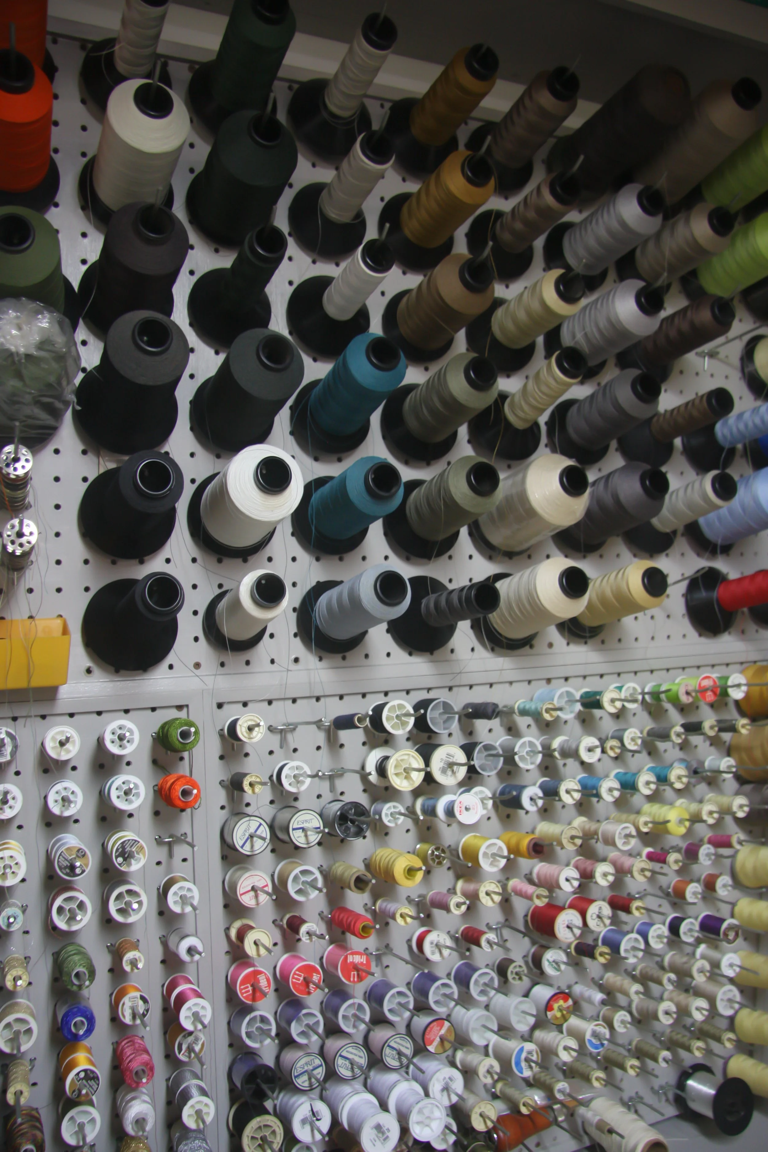 Display of numerous spools of thread in various colors on a pegboard wall, organized by size and color.