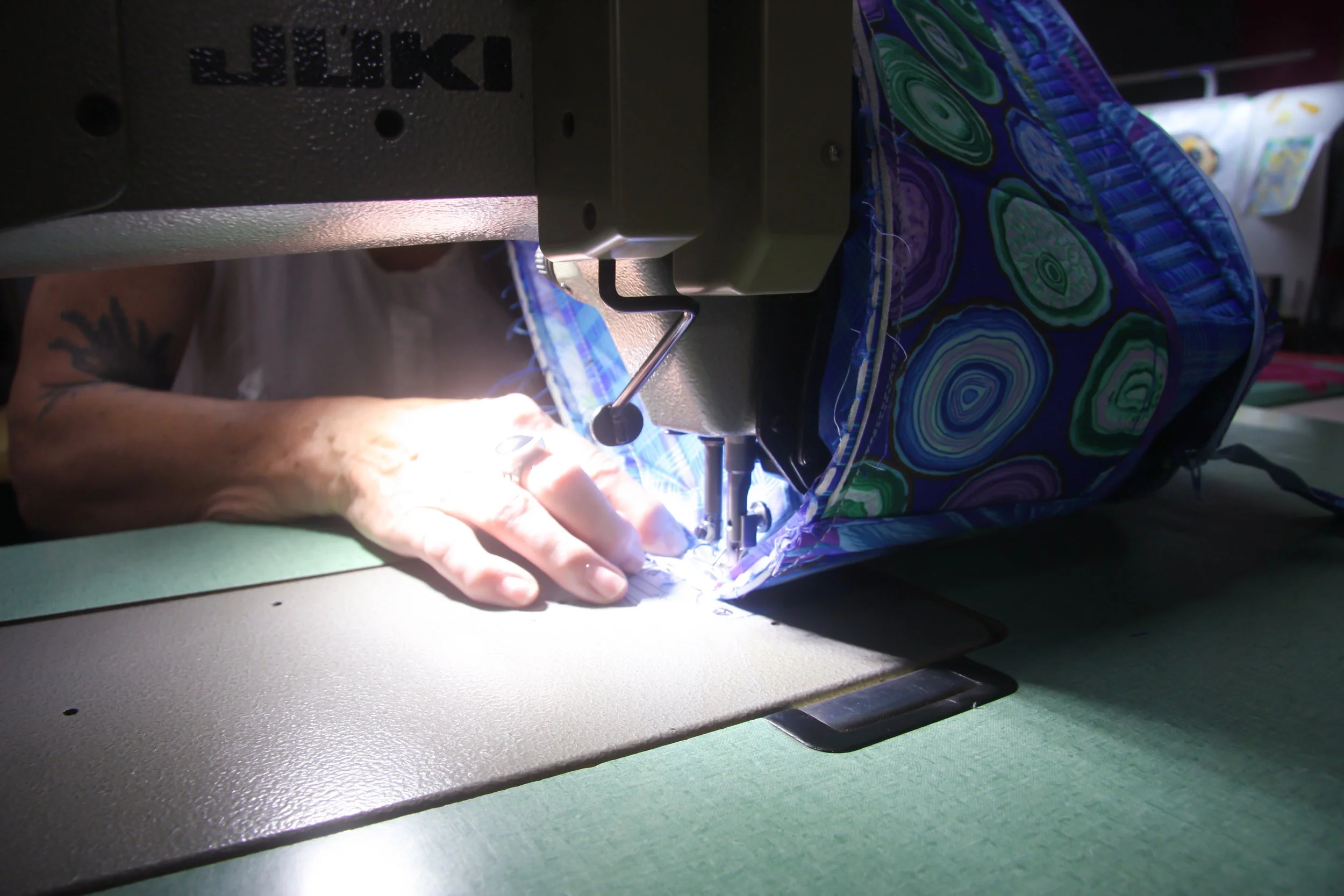 Close-up of a person sewing a colorful fabric bag with a sewing machine, their hand guiding the fabric.