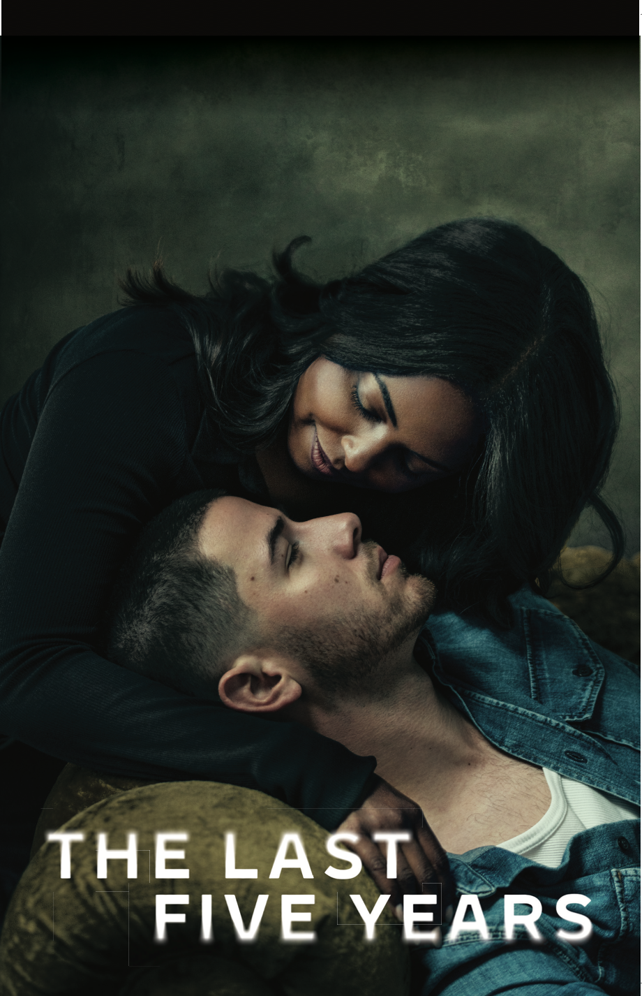 A woman with long black hair leaning over a man with short dark hair, lying on a yellow velvet sofa, close together in an intimate pose.