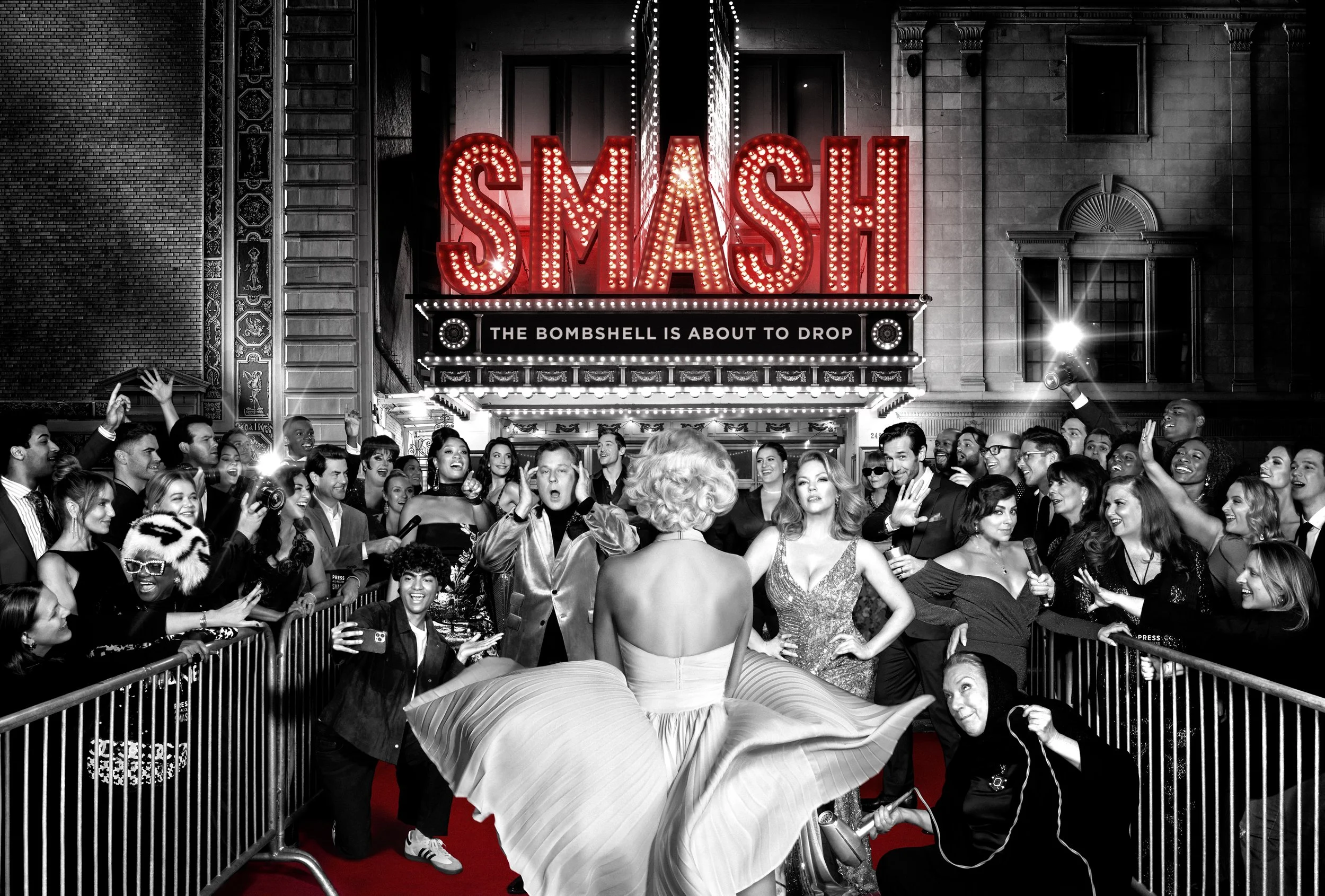 A woman walking on a red carpet in front of a large marquee sign with red letters spelling 'SMASH'. The sign also says 'The bombshell is about to drop'. The scene is in black and white, with audience members and photographers surrounding her, capturi