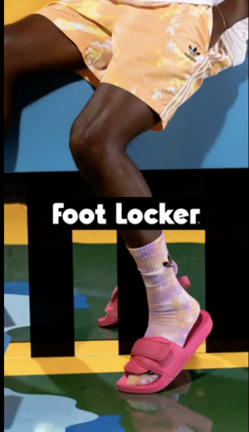 A person's leg and foot wearing pink sandals and colorful socks, with a Foot Locker logo overlay.