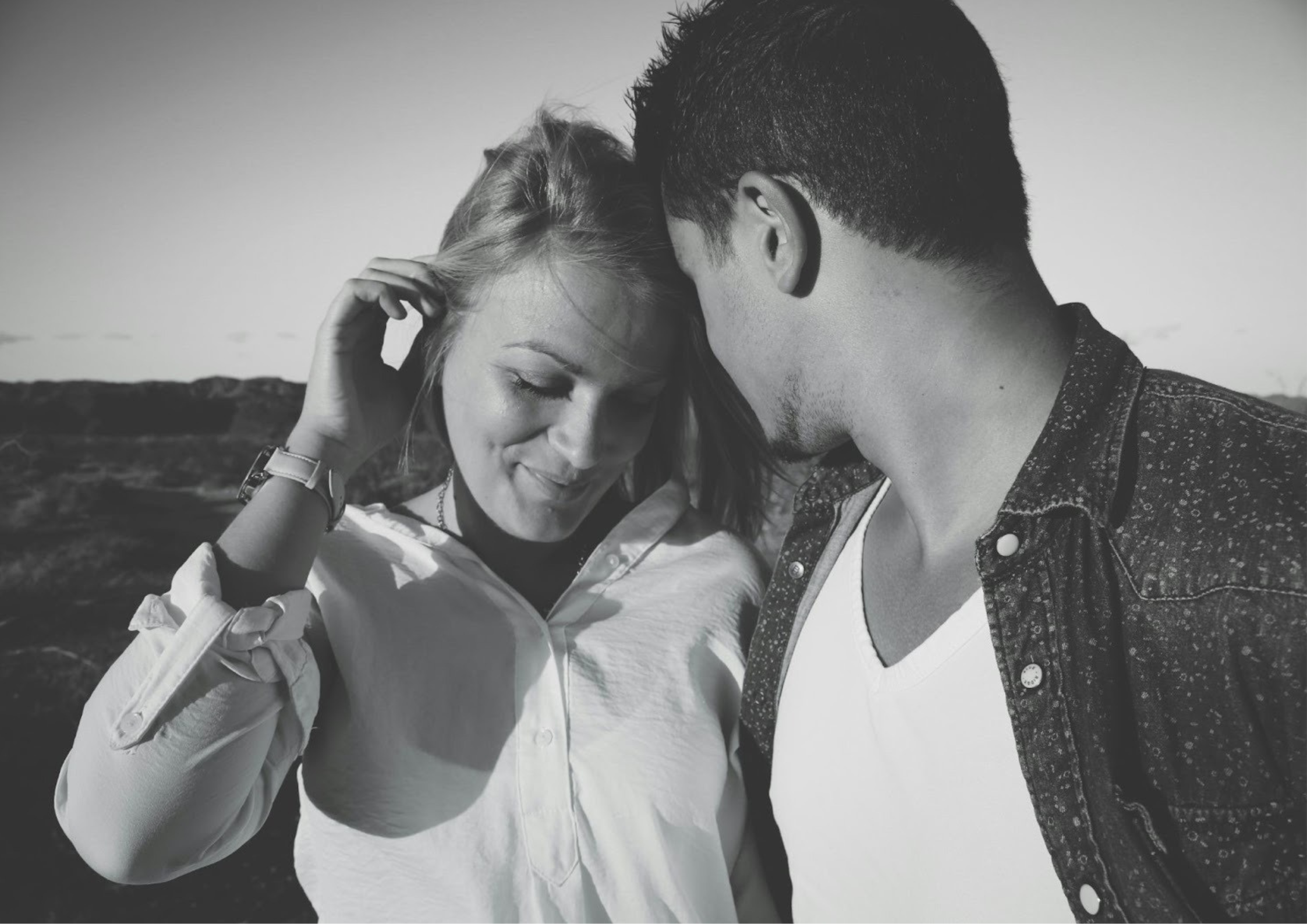 A couple standing close together, the woman smiling gently while the man leans toward her affectionately, capturing a tender and intimate moment.