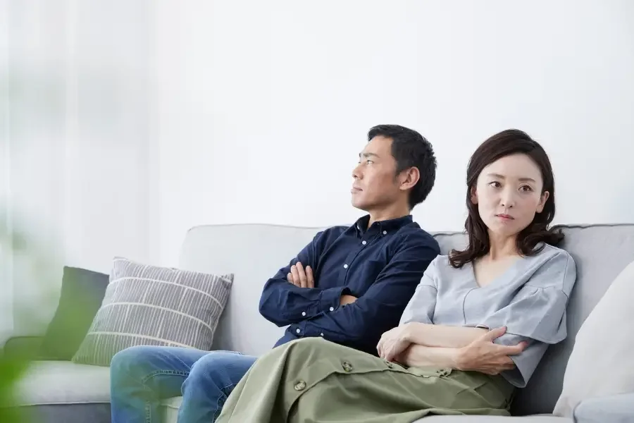 Couple sitting apart on a sofa with crossed arms, showing tension and emotional distance.