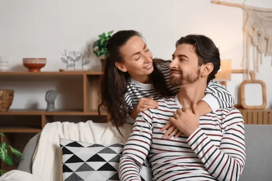 A man and woman in pajamas sit together on a couch, smiling and enjoying each other's company.