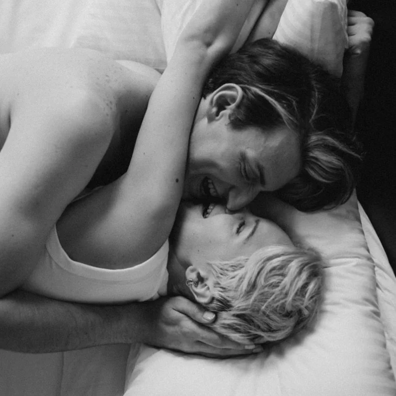 A couple playfully cuddling and laughing on a bed, sharing a sweet embrace.