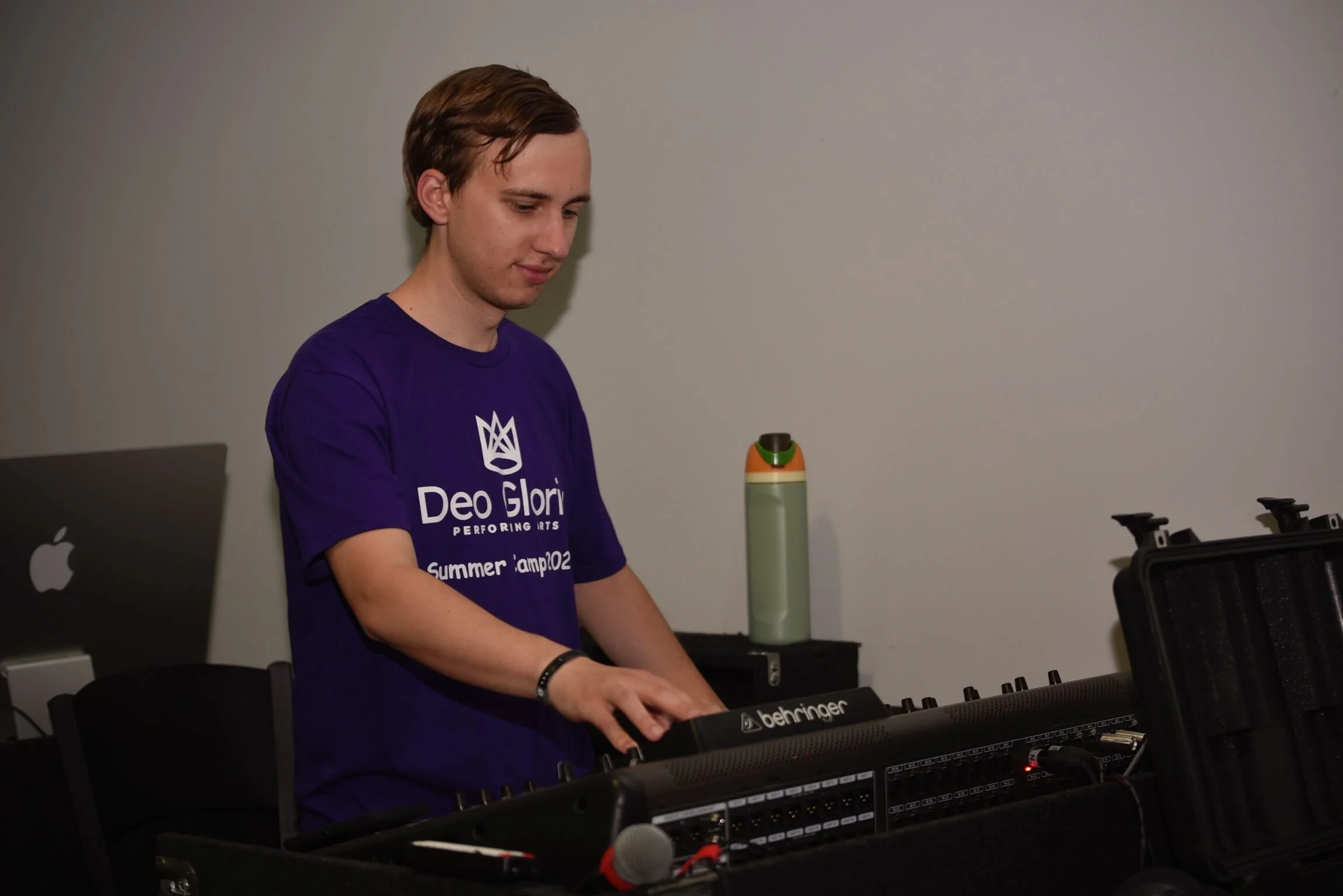 A young crew member in a purple t-shirt operating a Behringer sound mixing board.