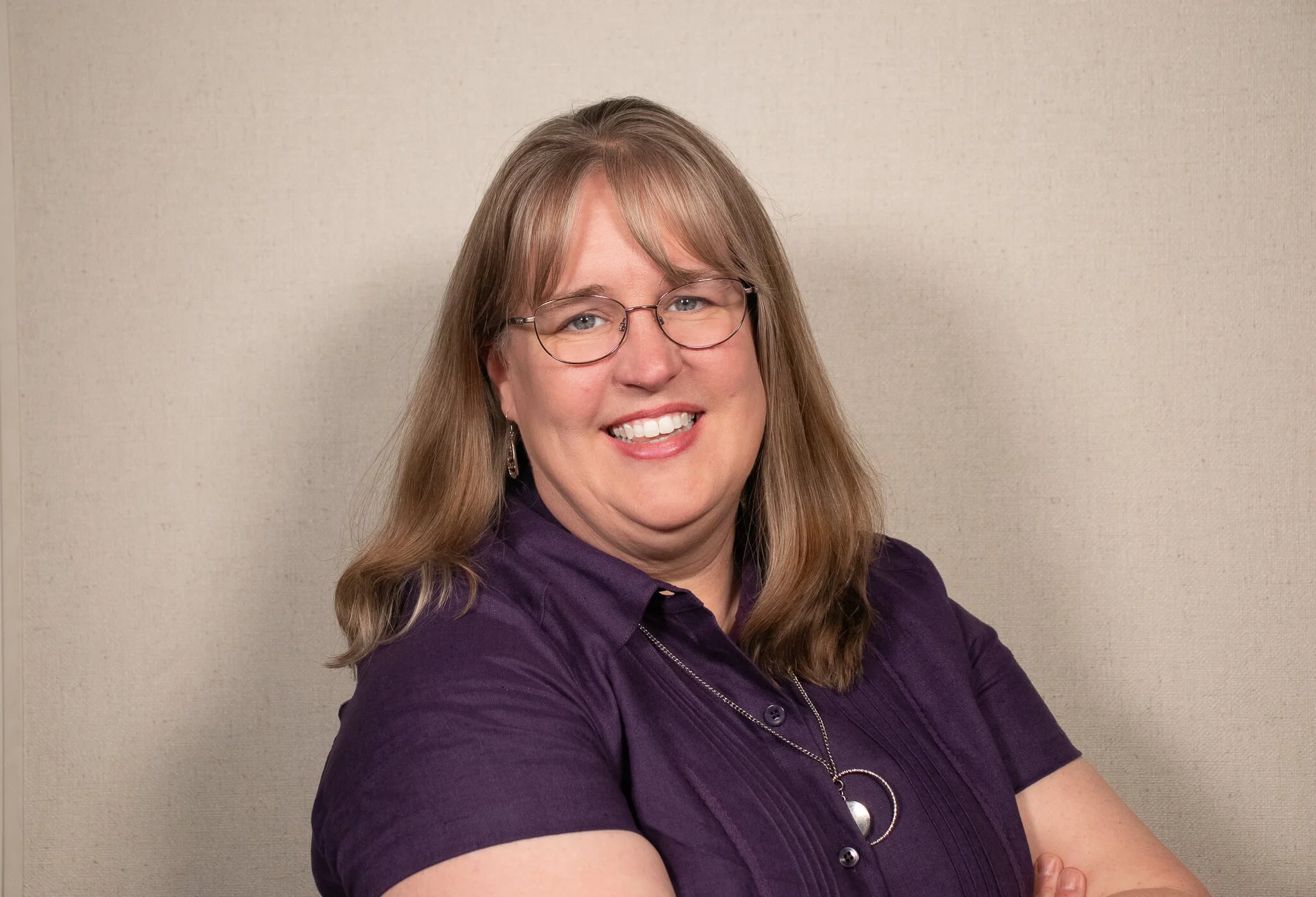 A headshot of a beautiful woman wearing purple and smiling at the camera
